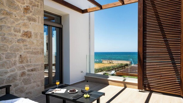 A balcony with a stone wall, a table with drinks, and a view of the sea.