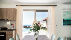 A modern kitchen with wooden cabinets, a dining table with chairs, a vase of flowers, and a view of a pool and ocean.