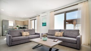 A modern living room with two grey sofas, a wooden coffee table, and a kitchen in the background.