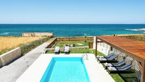 A pool with lounge chairs, a wooden pergola, and a view of the ocean.