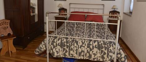 A bedroom with a bed, wooden wardrobe, and two framed portraits on the wall.