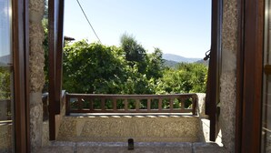 A stone staircase leading to a balcony with a wooden railing, surrounded by greenery and a clear sky.