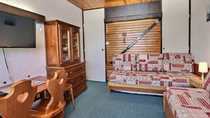 Ein gemütlicher Raum mit Holzboden, einem Bett mit gemusterten Betttextilien, einem Holzschrank, einem Schreibtisch mit Stuhl und einem an der Wand befestigten Fernseher.