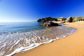 A beach with clear blue water, sandy shore, and rocky outcrops.