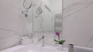 Un bagno moderno con un lavabo in marmo, uno specchio, un porta asciugamani e un'orchidea in vaso.