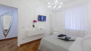 Una camera da letto moderna con un letto, una TV a parete, un tavolino consolle bianco, uno specchio e un lampadario.