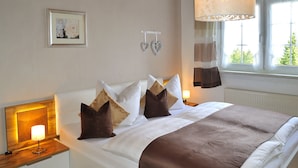 A neatly made bed with a brown and white bedspread, two bedside lamps, a framed picture on the wall, and a window with curtains. - Ferienwohnung An den Kurwiesen (Masserberg)