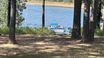 A lakeside view with a boat docked near the shore, surrounded by tall trees and grassy areas.