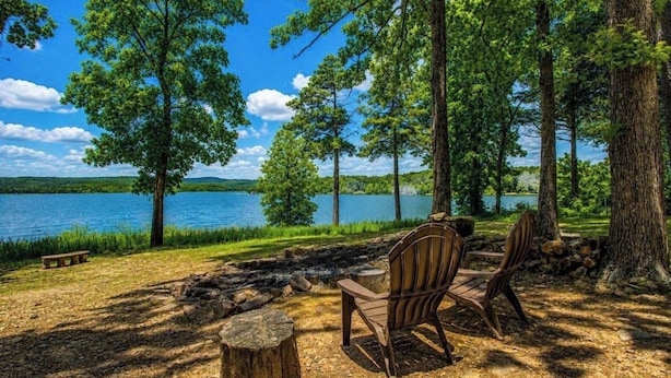Un terrain de camping au bord du lac, équipé d’un foyer, de deux fauteuils Adirondack et d’un banc.