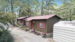 Une rangée de cabanes aux volets rouges, un espace extérieur abrité avec des sièges, et un chemin de gravier menant à l’entrée.