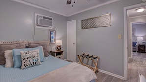 Une chambre à coucher comprenant un lit, un ventilateur de plafond, un climatiseur mural, une table de chevet avec une lampe et un élément décoratif fixé au mur.