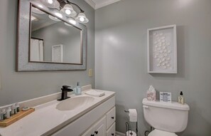 A bathroom with a white sink, a mirror, a toilet, and a framed artwork on the wall.