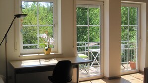 A room with a desk, chair, and two windows overlooking a balcony with a potted plant. - Ferienwohnung Buhl (Regensburg)
