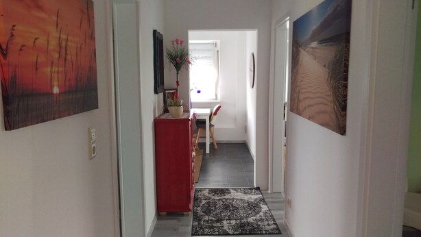 Um corredor com um armário vermelho, uma porta branca e um tapete preto e branco que leva a um quarto com uma porta branca.