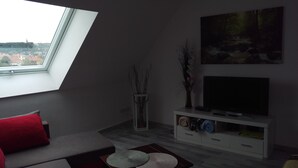 Uma sala de estar moderna com um claraboia, uma televisão de tela plana, um rack branco e um sofá vermelho.