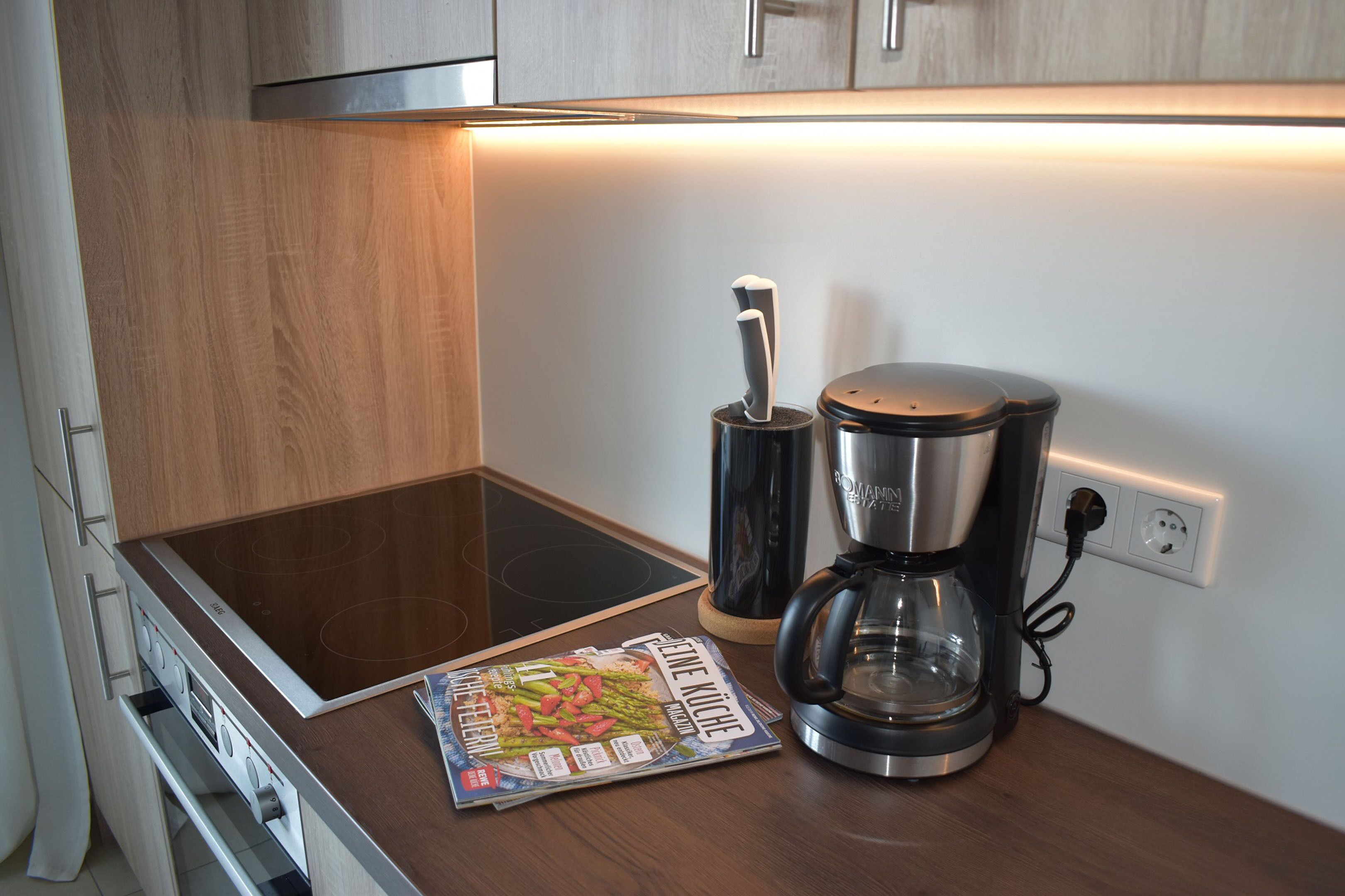 A kitchen with an induction cooktop, a coffee maker, and a magazine on the counter.