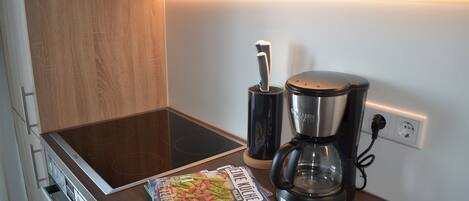 A kitchen with an induction cooktop, a coffee maker, and a magazine on the counter.