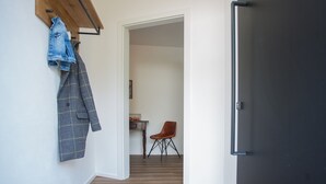 A hallway with a wooden coat rack, a plaid jacket, a brown chair, and a colorful rug. - Ferienwohnung Happyliving (Winterberg)