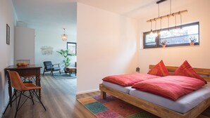 A bedroom with a bed, a desk, and a chair. There is a window with blinds and a hanging light fixture. - Ferienwohnung Happyliving (Winterberg)