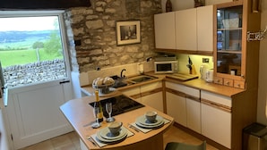 Una cocina con pared de piedra, una ventana con vistas al campo, un microondas y un armario de madera.