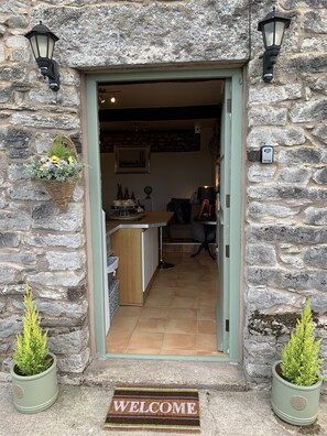 A stone building entrance with a welcome mat, a small reception desk, and two potted plants. - Characteristic & Cosy Self-contained 1 Bed Annexe (Kendal)