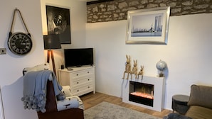 Una sala de estar con chimenea, televisor, reloj y un cuadro enmarcado de un paisaje urbano.