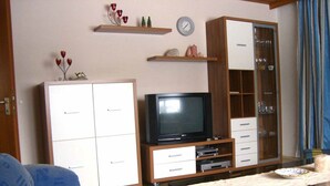 A living room with a sofa, a television, a cabinet, and a dining table. - Ferienwohnung Fürst (Mauth)