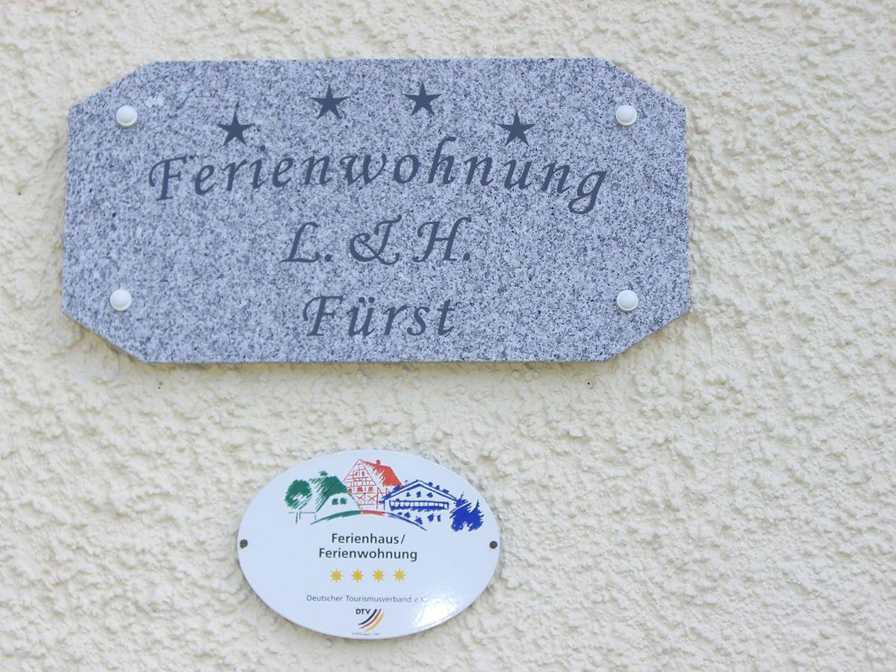 A sign for a guesthouse named 'Ferienwohnung L. & H. Fürst' with a badge below it indicating it is a member of the German Tourism Association.