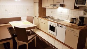 A compact kitchen with a dining area, including a table, chairs, a microwave, a stove, and a coffee maker. - Ferienwohnung Fürst (Mauth)