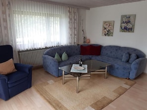 Una sala de estar con un sofá azul, una mesa de centro de vidrio, un sillón azul y un radiador.