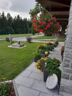 Un jardín ajardinado con un banco de piedra, un arreglo floral colgante y un monumento de piedra.