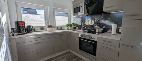 A modern kitchen with a built-in oven, microwave, and stainless steel appliances. There are two windows with decorative grills, a sink, and a countertop with various kitchen items.