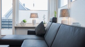 A modern living room with a grey sofa, two lamps, a potted plant, and a view of the outside through large windows. - Ferienwohnungen Citylight Winterberg (Winterberg)