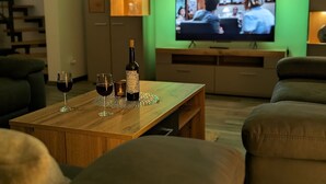 A living room with a wooden coffee table, two wine glasses, a bottle of wine, and a television displaying a show. - Ferienwohnungen Citylight Winterberg (Winterberg)