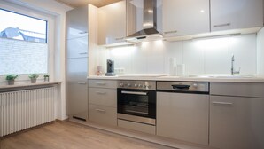 A modern kitchen with stainless steel appliances, a built-in oven, and a window with blinds. - Ferienwohnungen Citylight Winterberg (Winterberg)