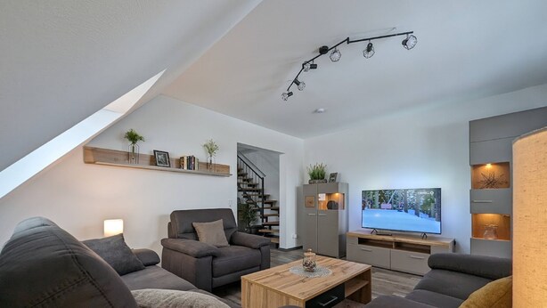 A modern living room with a sofa set, a coffee table, and a TV. There is a staircase leading to an upper level. - Ferienwohnungen Citylight Winterberg (Winterberg)