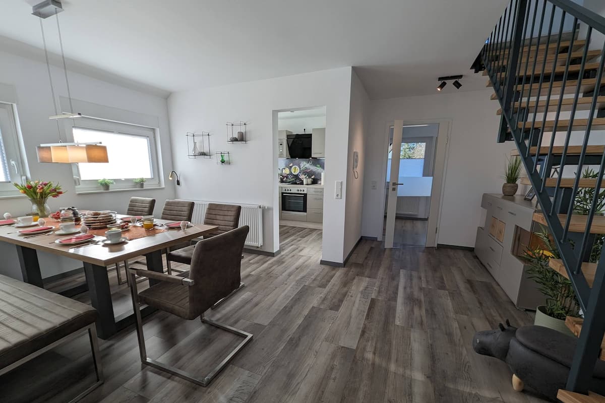 Une cuisine moderne avec un coin repas, un plancher en bois et un escalier.