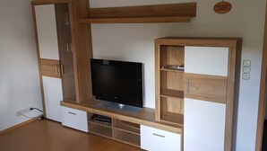 Un meuble de rangement moderne pour appareils multimédias, doté d’un téléviseur à écran plat, d’étagères en bois et de compartiments de rangement intégrés.