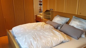 Un lit bien fait, avec une couette blanche et beige, une tête de lit en bois et une table de chevet avec une lampe.