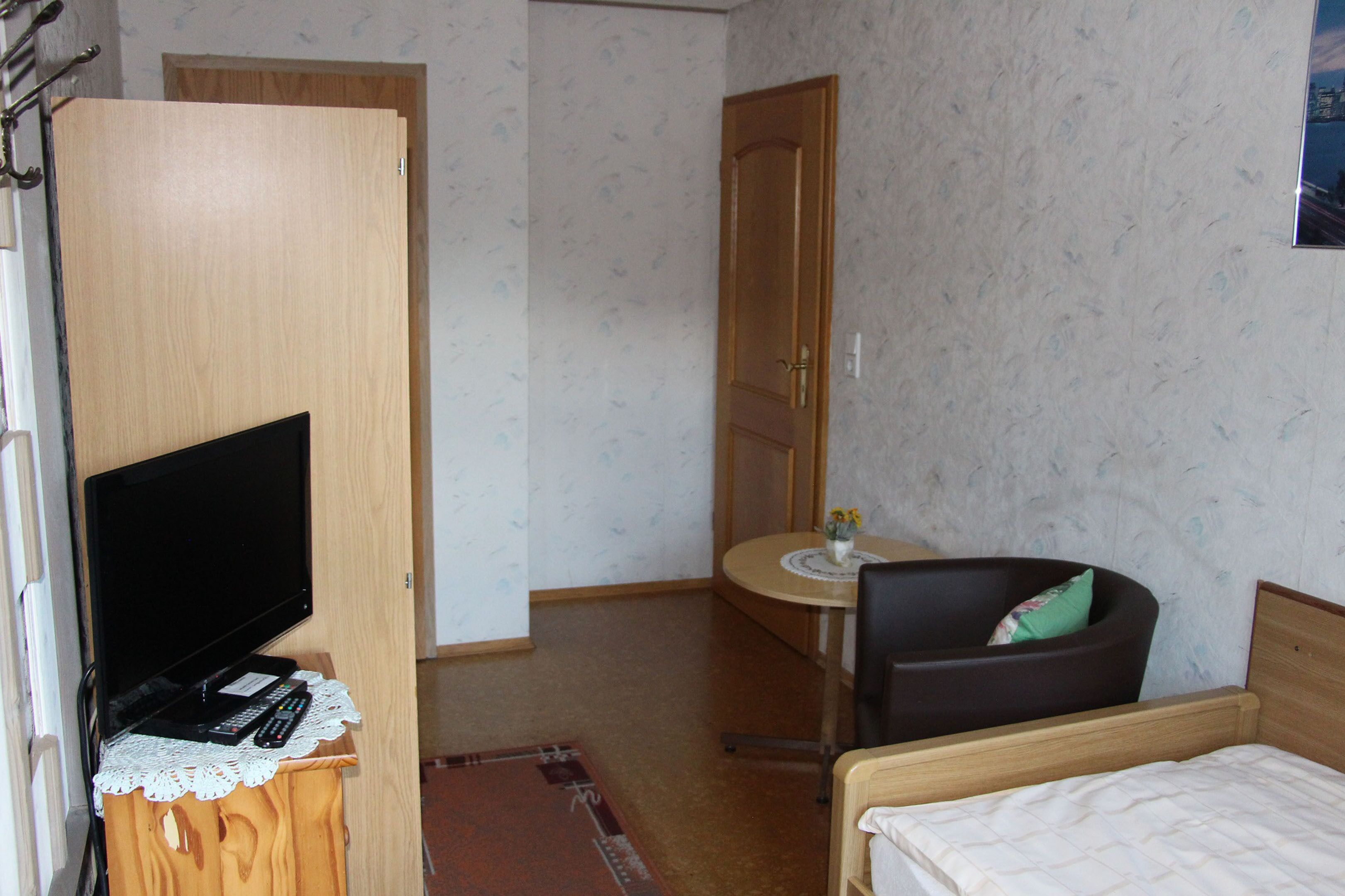 Una habitación pequeña con una cama, un escritorio con una silla, un televisor sobre un mueble bajo y un armario.