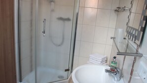 Un baño moderno con cabina de ducha de vidrio, un lavamanos blanco y toallas ordenadamente apiladas.