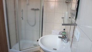 Un baño con ducha de vidrio, un lavamanos blanco con espejo y un perchero con toallas dobladas.