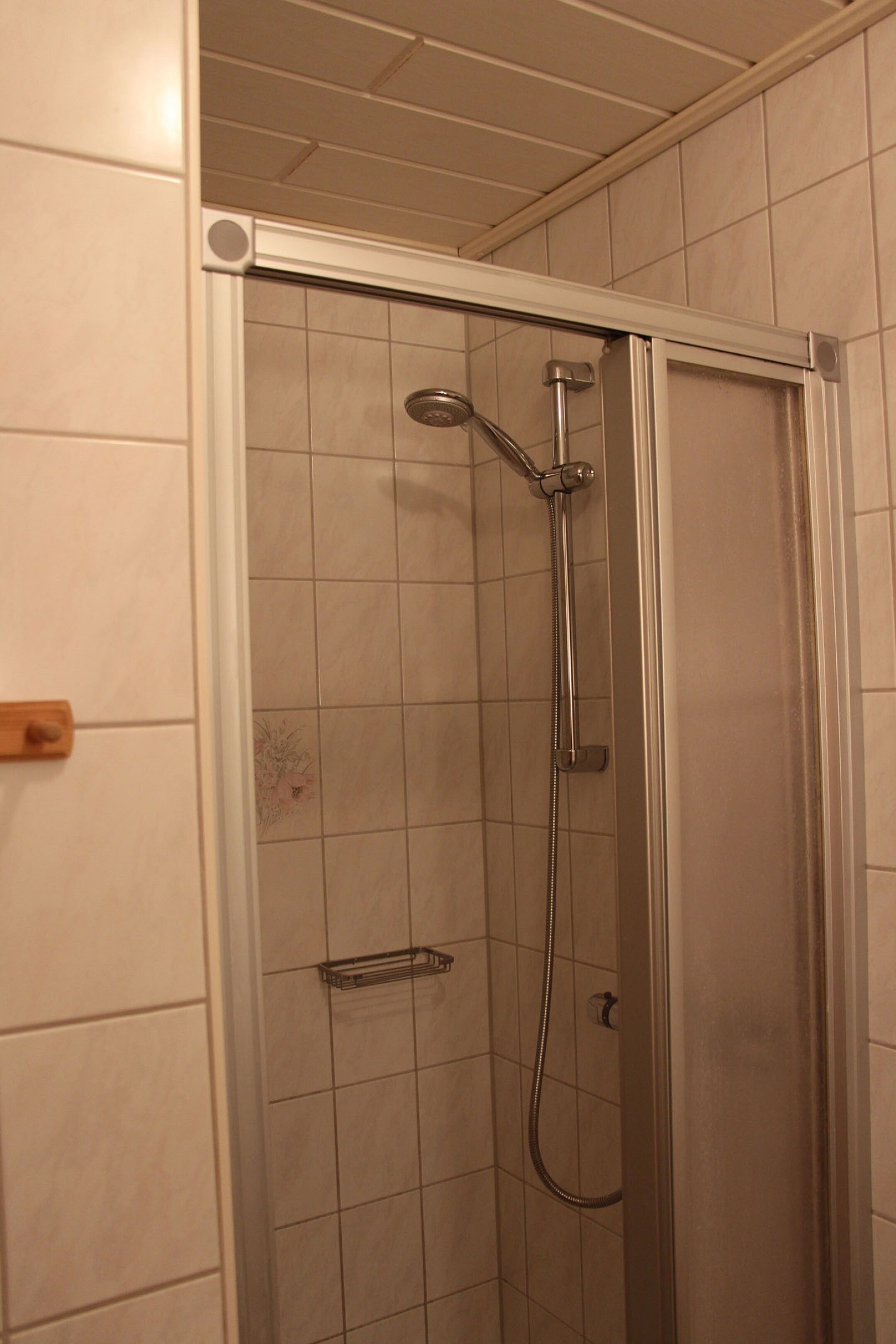A shower with a glass door, tiled walls, and a metal showerhead.