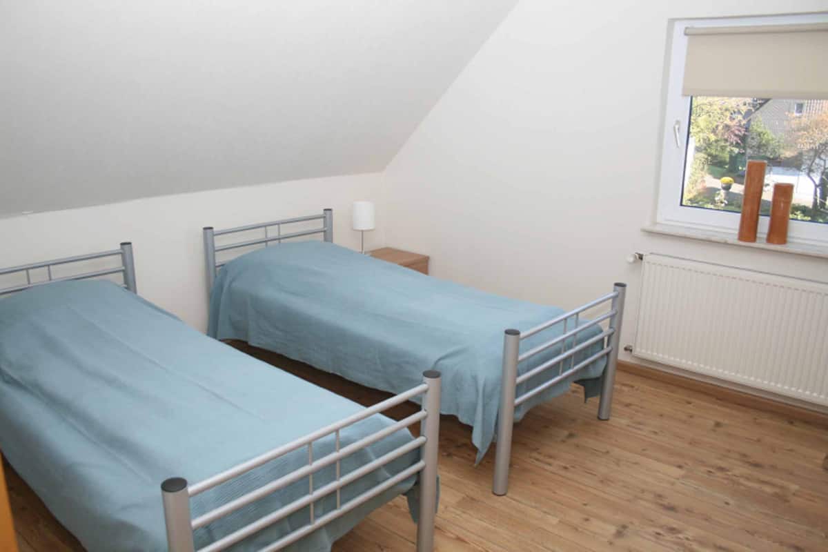 Quarto pequeno com duas beliches de metal, uma janela com vista para o exterior e um radiador na parede.