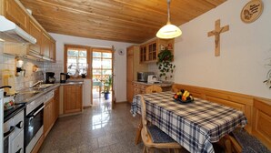 A kitchen with wooden cabinets, a dining table with a checkered tablecloth, and a cross on the wall. - Ferienhof Degenhart (Mauth)