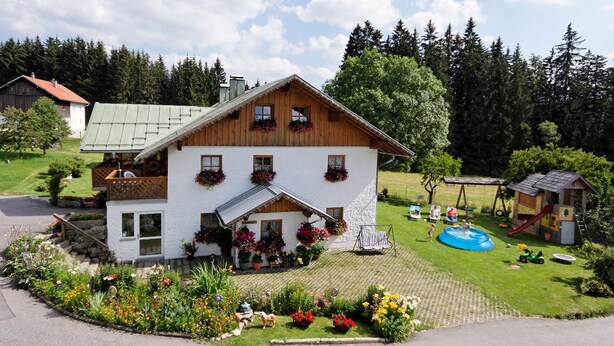 A two-story chalet with a balcony, surrounded by a well-maintained garden and a children's play area. - Ferienhof Degenhart (Mauth)