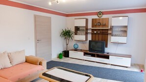Una sala de estar con sofá, televisor, mueble de entretenimiento y una pequeña mesa.