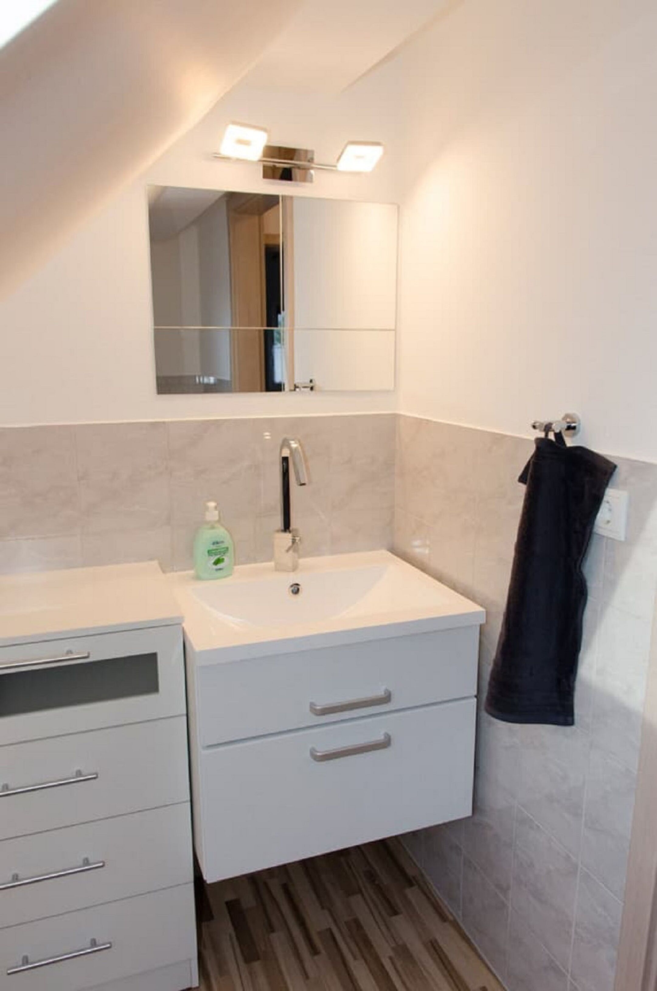 A modern bathroom with a white vanity, a mirror, and a towel rack.