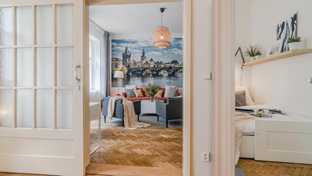 A modern living room with a herringbone floor, a large window with frosted glass, a cityscape mural, and a dining area with a table and chairs. - APT in Center Prague by Michal&Friends (Prague)