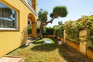 Um pátio com uma árvore, uma parede coberta por plantas trepadeiras e um edifício com um arco.